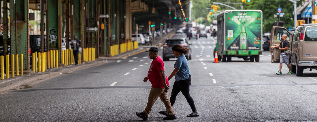 Two pedestrians cross a street with heavy traffic in the background