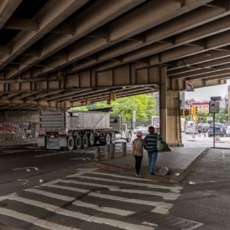 Two people walk in a crosswalk under the elevated BQE in Williamsburg, Brooklyn